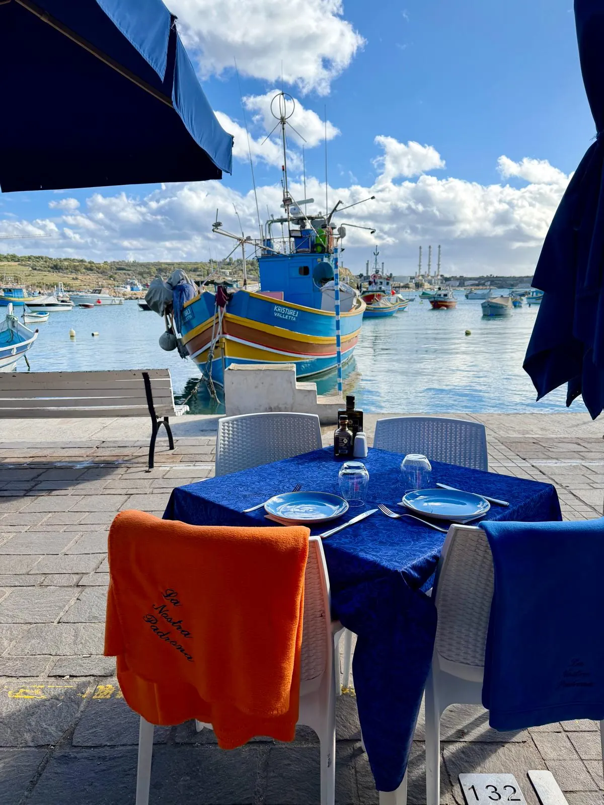 A table on the harbour with a luzzu boat behind it