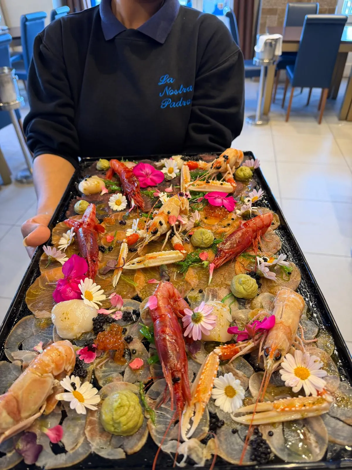 A server carrying a large crudo platter decorated with flowers